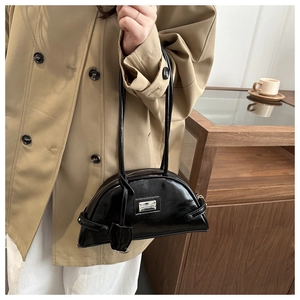Detail of black patent leather shoulder bag with metallic logo plate and stylish handles