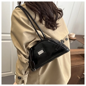 Detail of a black patent leather shoulder bag with a metallic logo and sleek zipper