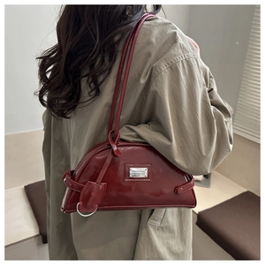Detail of burgundy semi-circle shoulder bag featuring a silver logo plate on glossy leather