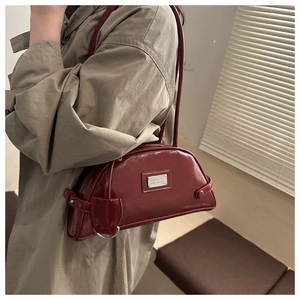 Close-up of burgundy patent leather shoulder bag with glossy finish and metal plaque