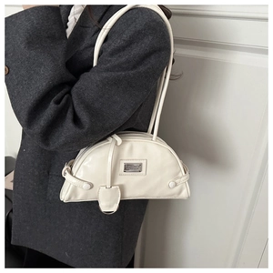 Detail of cream crescent shoulder bag with metallic plaque on sleek gray suit jacket