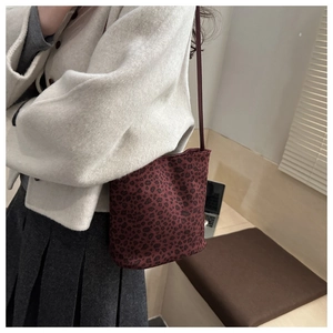 Dettaglio di una borsa a secchiello bordeaux con stampa leopardata indossata a spalla