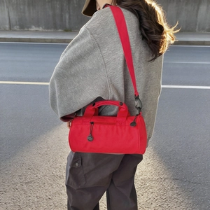 Sac de fitness cylindrique rouge avec bandoulière présenté dans un décor de rue urbain