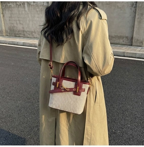 Detail of canvas bucket bag with burgundy leather trim and gold metal buckle hardware