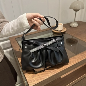 Sac à bandoulière plissé noir avec nœud et étoiles argentées dans un décor cosy