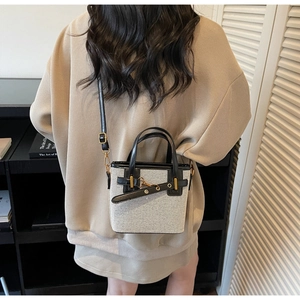 Detail of canvas bucket bag with black leather trim and metal clasp on beige sweater