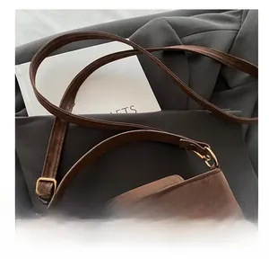 Detail of dark brown suede crossbody bag with gold V-shaped logo and adjustable strap