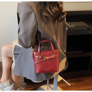 Detail of burgundy glossy leather bucket bag featuring gold buckle and Maven & Chic logo