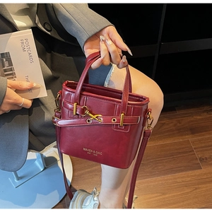 Detail of burgundy leather bucket bag with gold MAVEN & CHIC branding and metal buckle