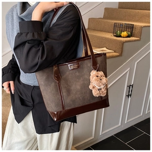 Detail of dark brown tote bag with cartoon cat print and plush dog charm accessory