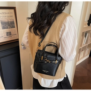 Detail of a black bucket bag with gold metal clasp and Maven & Chic brand logo