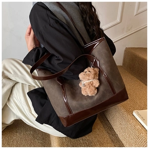 Detail of a large brown embossed tote bag with glossy leather handles and plush bear charm