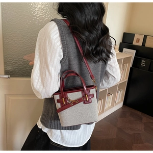 Detail of red leather trim and gold horsebit buckle on a grey canvas bucket bag