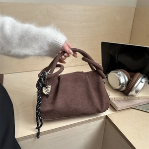 Sac à main plissé en daim marron avec breloque cœur sur un bureau en bois clair
