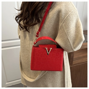 Detail of red square handbag with animal texture, gold V hardware on beige coat