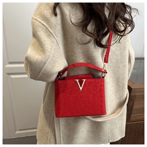 Detail of red square handbag with gold V metal hardware and leopard texture finish