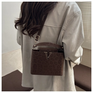 Detail of a brown leopard print shoulder bag with gold V-shaped logo on a textured surface