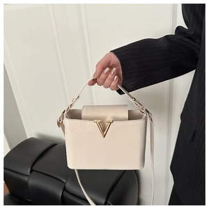 Detail of a beige trapezoid handbag featuring a gold V-shaped buckle and top handle