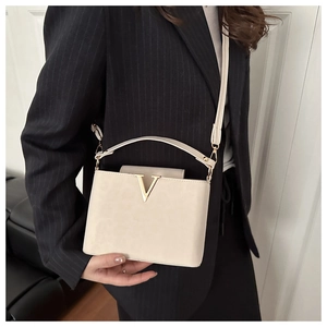 Detail view of cream square handbag with gold V logo worn crossbody by a model in a suit
