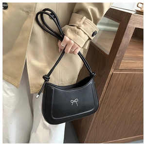 Close-up of black leather shoulder bag featuring a decorative silver metal bow detail