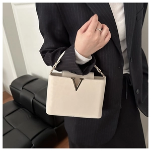Detail of cream leather handbag with gold V-shape hardware on black striped blazer