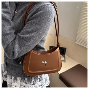 Detail of brown leather crescent bag featuring a stylish silver bow and knotted strap