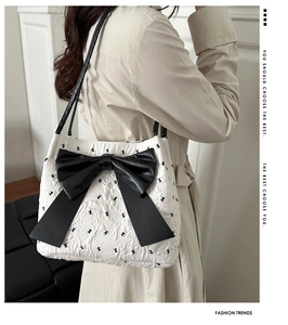 Model view of white quilted bucket bag with large black bow and textured fabric details