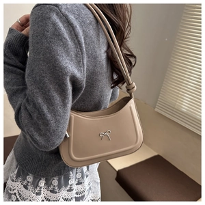 Detail of beige leather bag with a silver metallic bow and knotted strap design