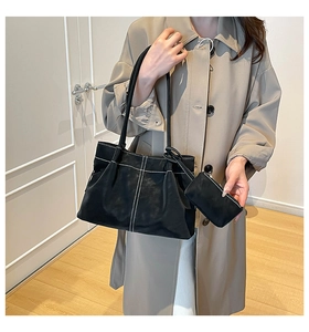 Close-up of black suede tote bag with white contrast stitching and matching small pouch