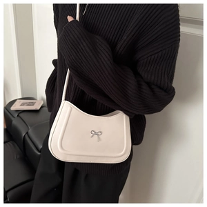 Close-up of beige half-moon shoulder bag with a metallic bow on black knitwear