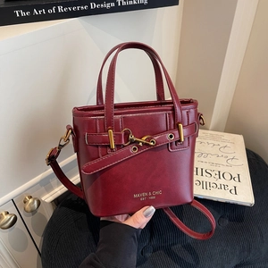 Elegant wine red bucket bag with gold lettering and top handle on a textured background
