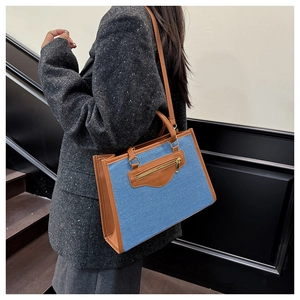 Détail du sac cabas en jean bleu avec lanières en cuir marron et poche dorée zippée