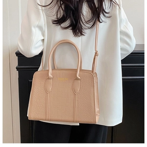 Detail of beige crocodile pattern handbag with golden fashion lettering and top handle