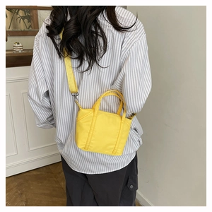 Rear view of a model carrying the bright yellow nylon mini tote bag with crossbody strap