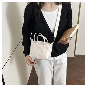 Model wearing a minimalist cream nylon crossbody bag with wide fabric shoulder strap