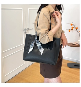 Dettaglio della borsa tote in pelle nera con un foulard di seta blu avvolto sul manico