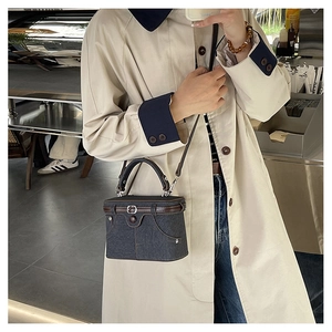 Detail of dark blue denim box bag with brown leather trim worn as a crossbody by a model