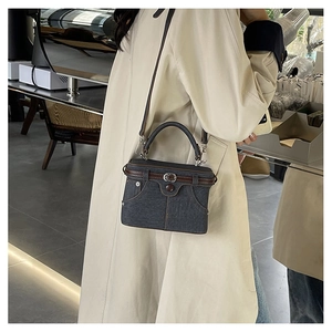 Detail showing creative denim box bag with leather trim on model in a cafe setting