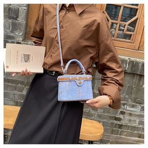 Detail of light blue denim cylinder bag with brown leather belts and rivets