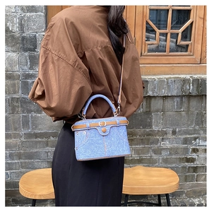 Outdoor shot of a blue denim box bag with brown leather trim and retro buckle details