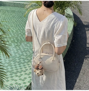 Gros plan du sac boston en cuir blanc crème avec bandoulière et charm de caniche mignon