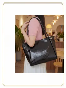 Detail of a large black leather tote bag with glossy finish on a shoulder strap
