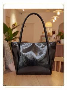 Glossy black patent leather tote bag on a wooden table in a warm cafe setting
