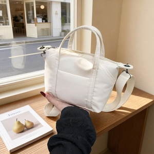Minimalist white nylon crossbody bag with wide shoulder strap in a cafe setting
