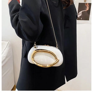 Detail of white oval clutch bag with large gold U-shaped buckle and metal chain strap