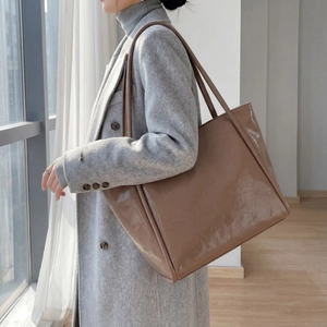Brown glossy patent leather tote bag detail on shoulder of model in grey coat
