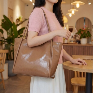 Lifestyle view of a glossy brown leather tote bag with double straps on a model in a cafe