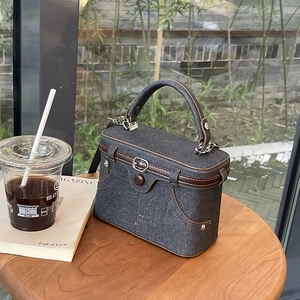 Retro denim box handbag with brown leather trim on wooden table with outdoor cafe view