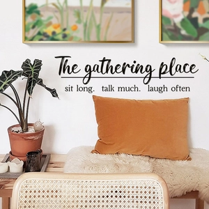 Close-up of 'The gathering place' wall sticker in a warm living room with rattan chair