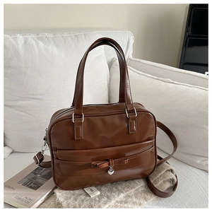 Detailed view of dark brown leather handbag with metal heart charm and bow on white sofa